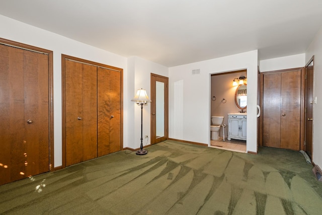 unfurnished bedroom featuring ensuite bathroom, dark carpet, and two closets