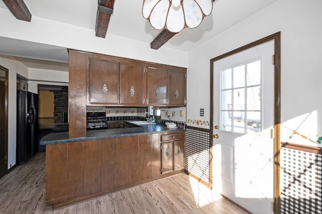 kitchen featuring black fridge, light wood-type flooring, kitchen peninsula, beam ceiling, and decorative backsplash