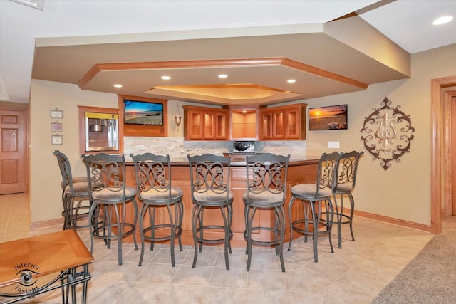 bar featuring tasteful backsplash, a raised ceiling, and light tile patterned floors