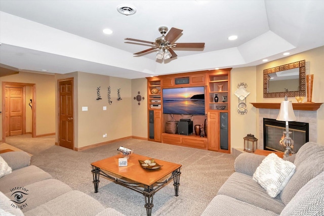 carpeted living room with ceiling fan, built in shelves, a fireplace, and a tray ceiling