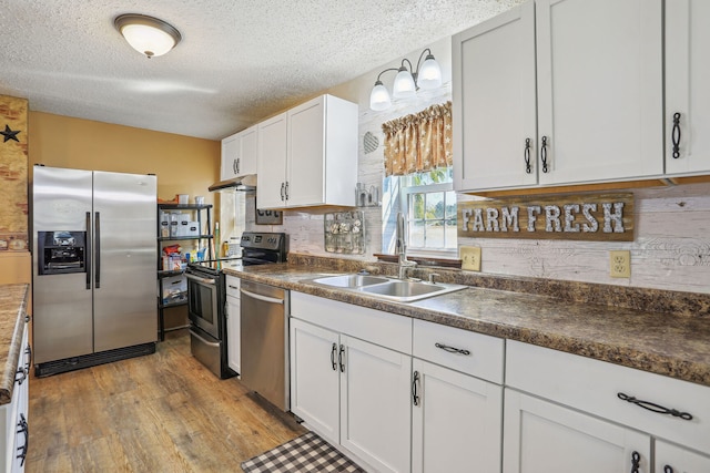 kitchen with appliances with stainless steel finishes, white cabinets, a textured ceiling, light hardwood / wood-style flooring, and sink