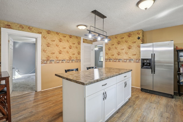 kitchen featuring stainless steel fridge, dark wood-type flooring, white cabinets, a kitchen island, and decorative light fixtures