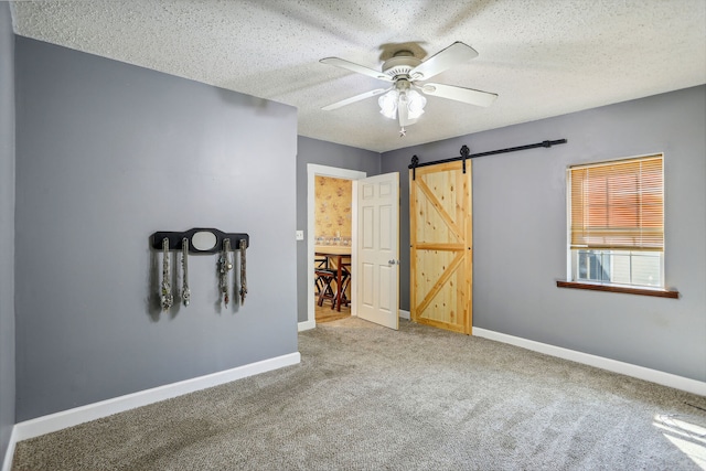 unfurnished room with a barn door, carpet, a textured ceiling, and ceiling fan