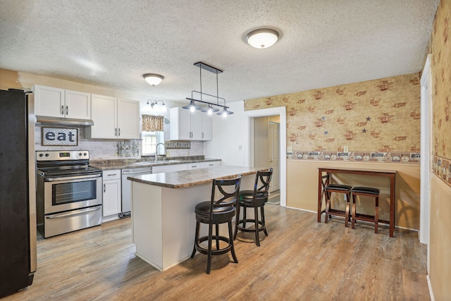 kitchen featuring sink, white cabinetry, hanging light fixtures, light hardwood / wood-style flooring, and stainless steel appliances