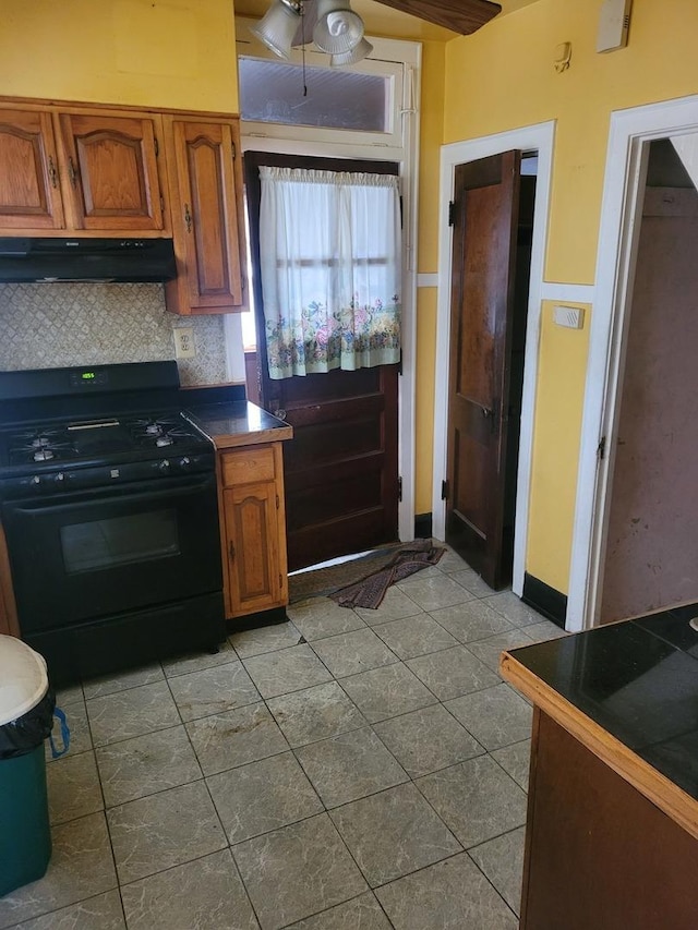 kitchen with brown cabinets, dark countertops, tasteful backsplash, gas stove, and under cabinet range hood