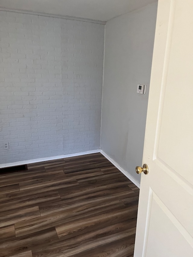 unfurnished room with brick wall and dark wood-type flooring