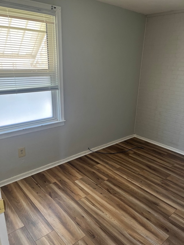 unfurnished room featuring wood-type flooring and brick wall