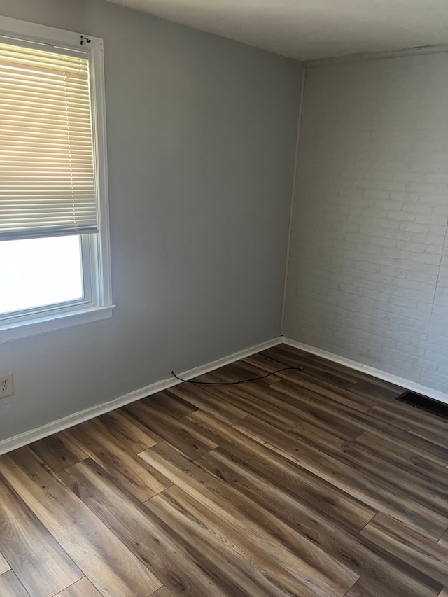 spare room with dark hardwood / wood-style floors and brick wall