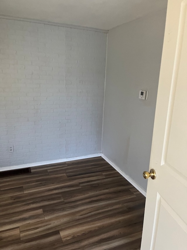 spare room with dark hardwood / wood-style flooring and brick wall