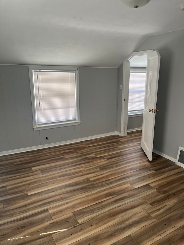 empty room featuring dark wood-type flooring, vaulted ceiling, and plenty of natural light