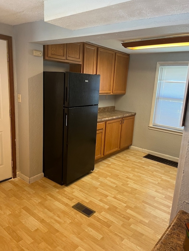 kitchen featuring black refrigerator, a textured ceiling, and light hardwood / wood-style flooring