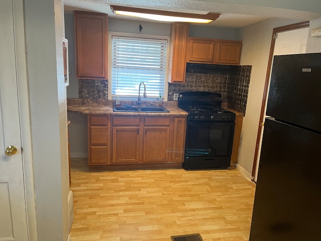 kitchen with black appliances, light hardwood / wood-style flooring, range hood, sink, and decorative backsplash