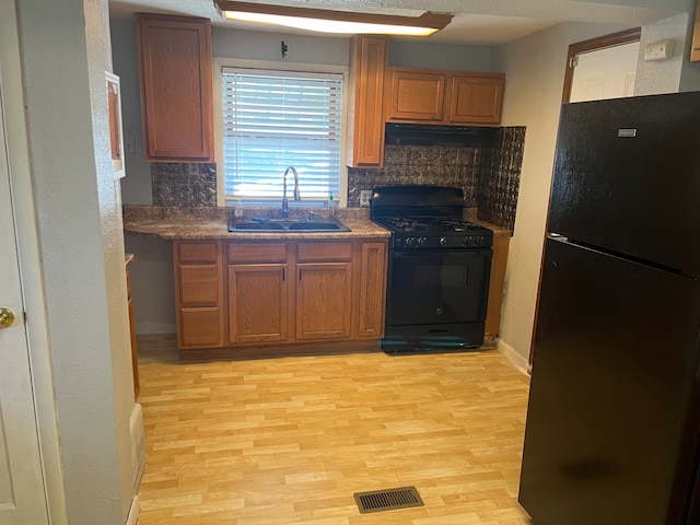 kitchen featuring black appliances, decorative backsplash, light hardwood / wood-style floors, and sink