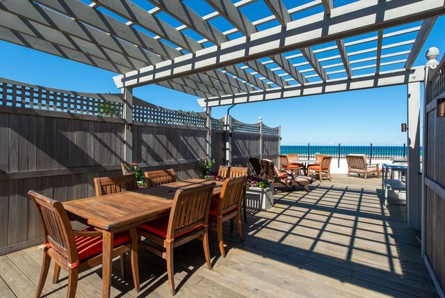 wooden deck featuring a water view, a pergola, and a beach view