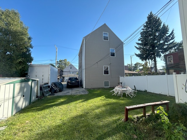 rear view of house featuring a lawn and a storage unit