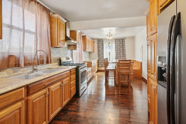 kitchen featuring dark wood-type flooring, stainless steel appliances, wall chimney exhaust hood, and a notable chandelier