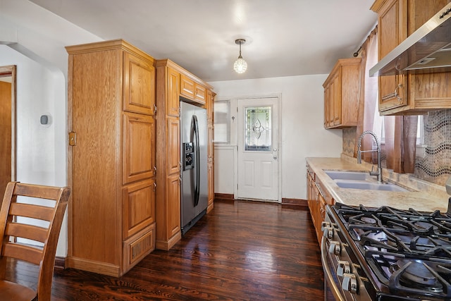 kitchen with appliances with stainless steel finishes, sink, wall chimney range hood, dark hardwood / wood-style floors, and pendant lighting