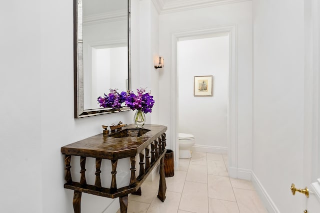 half bathroom featuring toilet, ornamental molding, a sink, tile patterned flooring, and baseboards