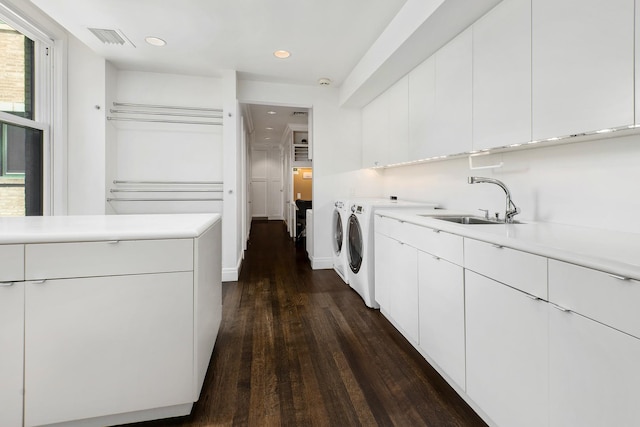 clothes washing area featuring visible vents, cabinet space, a sink, dark wood-type flooring, and washer and clothes dryer