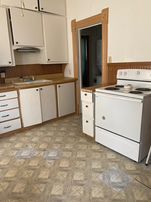 627 Hennepin St, Lasalle, IL 61301 - kitchen with a wainscoted wall, white cabinets, white electric range, a sink, and stacked washer and dryer