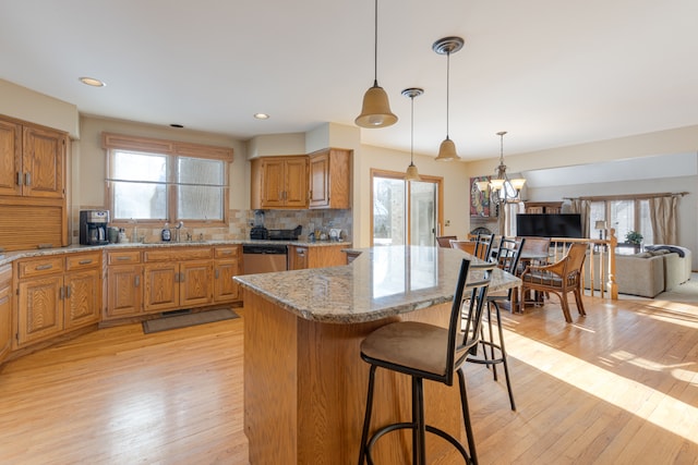 kitchen featuring light wood-type flooring, a wealth of natural light, a chandelier, and a breakfast bar