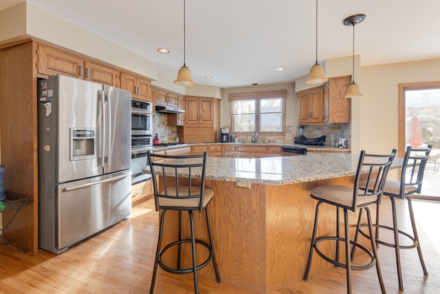 kitchen with backsplash, hanging light fixtures, stainless steel appliances, and light hardwood / wood-style flooring