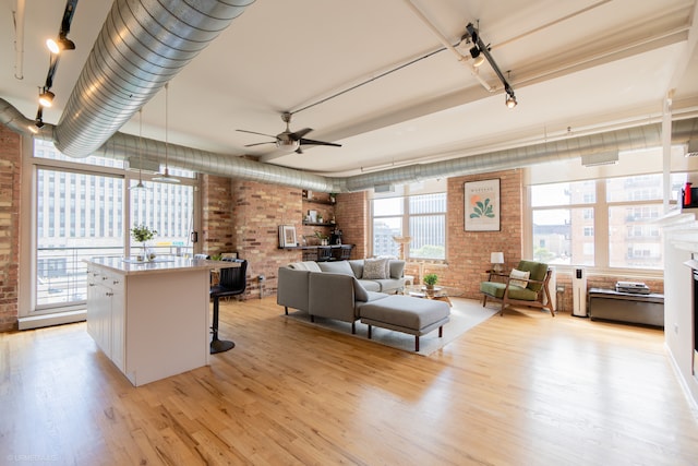 living room with a wealth of natural light, brick wall, ceiling fan, and light hardwood / wood-style floors