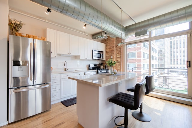 kitchen featuring white cabinets, light wood-type flooring, appliances with stainless steel finishes, a kitchen island, and decorative backsplash