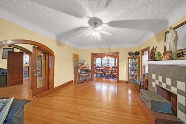 interior space with light wood-type flooring, ceiling fan with notable chandelier, a textured ceiling, and a tile fireplace