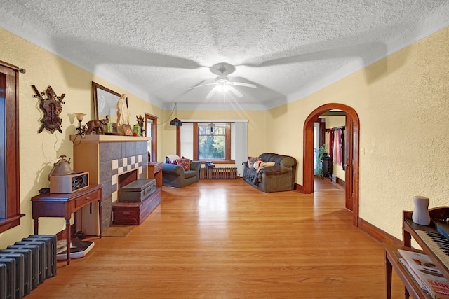 living room featuring ceiling fan, a textured ceiling, radiator heating unit, light hardwood / wood-style flooring, and a tile fireplace