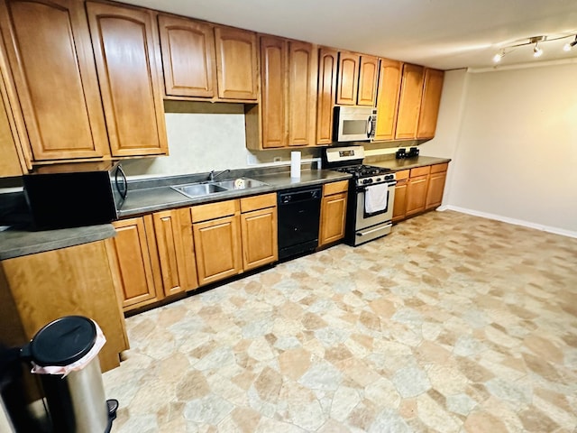 kitchen featuring appliances with stainless steel finishes, dark countertops, a sink, brown cabinetry, and stone finish flooring