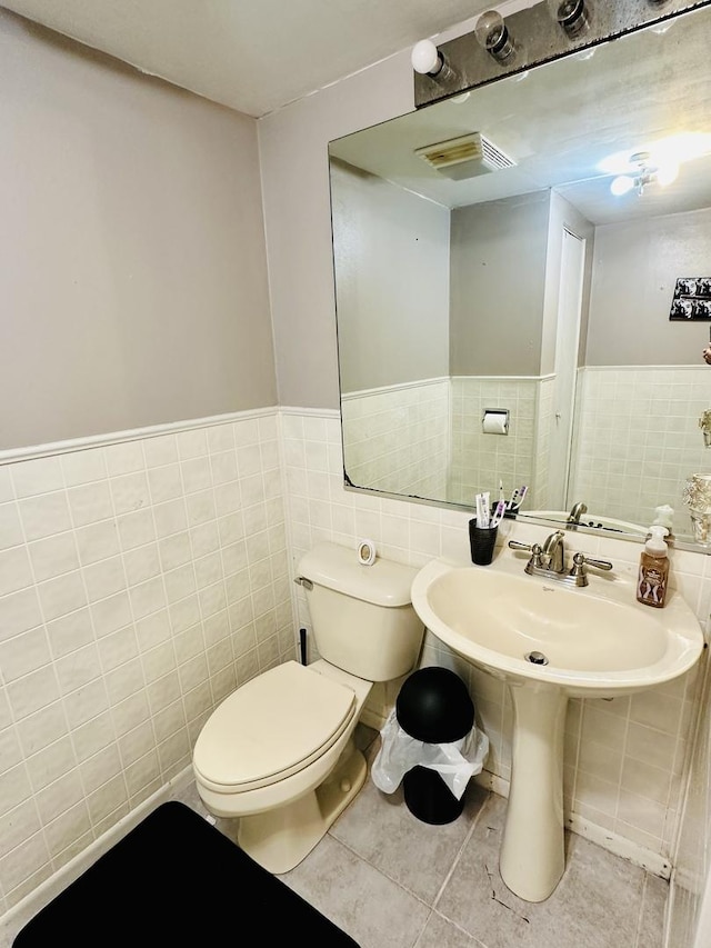 bathroom featuring tile walls, toilet, tile patterned floors, and a wainscoted wall