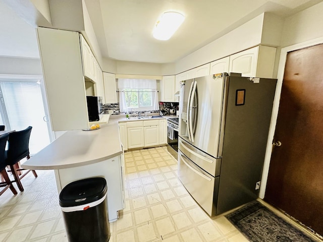 kitchen featuring stainless steel appliances, light floors, a peninsula, light countertops, and white cabinetry
