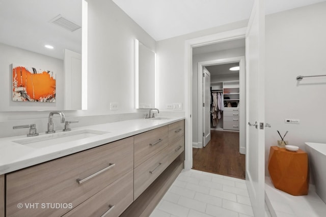 bathroom featuring visible vents, a walk in closet, a freestanding tub, a sink, and double vanity