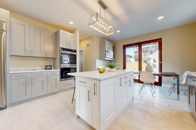 kitchen with gray cabinets, stainless steel double oven, hanging light fixtures, and a center island