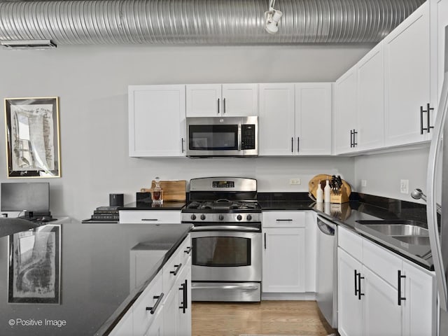 kitchen featuring appliances with stainless steel finishes, light wood-type flooring, sink, dark stone countertops, and white cabinets