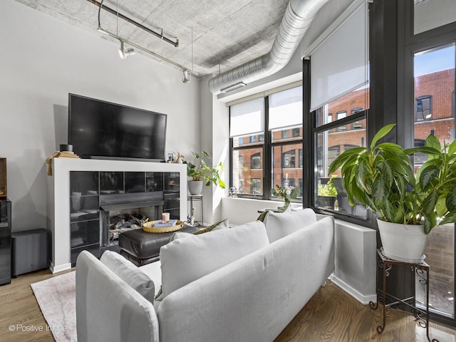 living room with a tile fireplace, a wealth of natural light, rail lighting, and hardwood / wood-style flooring