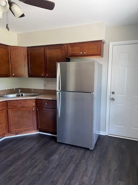 kitchen with stainless steel refrigerator, backsplash, sink, ceiling fan, and dark wood-type flooring