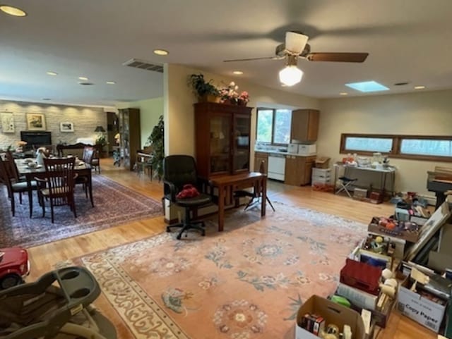 living room with light hardwood / wood-style flooring, a skylight, and ceiling fan