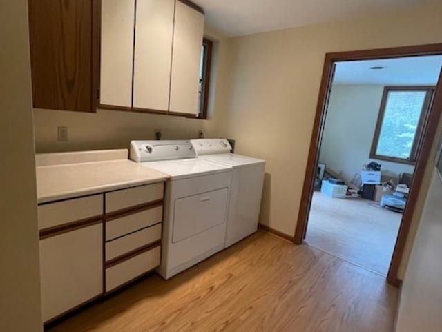 clothes washing area with cabinets, washer and clothes dryer, and light wood-type flooring