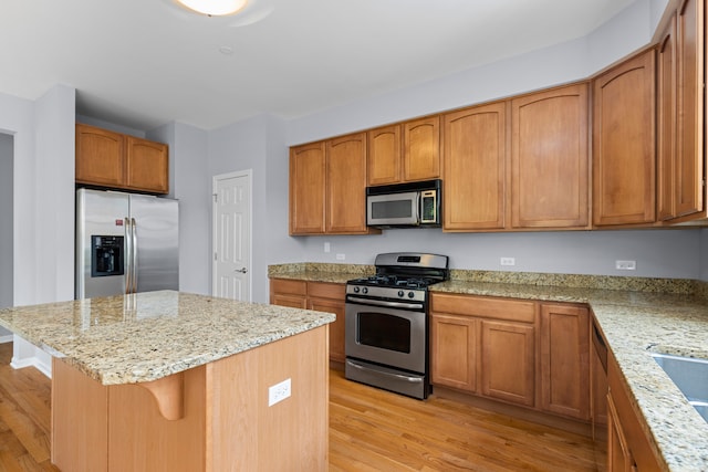 kitchen featuring light wood-type flooring, a center island, light stone counters, and stainless steel appliances