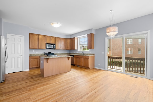 kitchen with a kitchen island, pendant lighting, a notable chandelier, light hardwood / wood-style floors, and stainless steel appliances