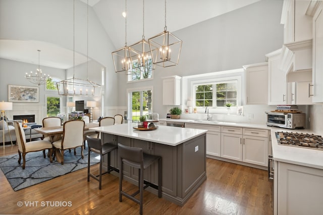 kitchen with a kitchen breakfast bar, decorative light fixtures, high vaulted ceiling, stainless steel gas stovetop, and white cabinets