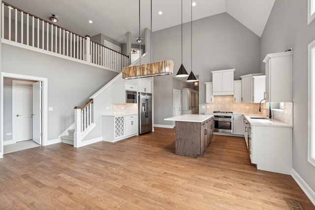 kitchen with stainless steel appliances, high vaulted ceiling, a center island, white cabinets, and light wood-type flooring