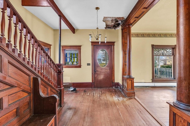 entrance foyer featuring a notable chandelier, light hardwood / wood-style floors, beam ceiling, and decorative columns