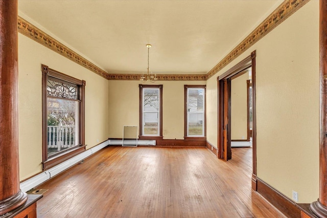 empty room featuring light hardwood / wood-style floors, an inviting chandelier, a wealth of natural light, and decorative columns