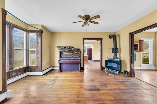 misc room featuring a wood stove, hardwood / wood-style flooring, a baseboard radiator, and ceiling fan