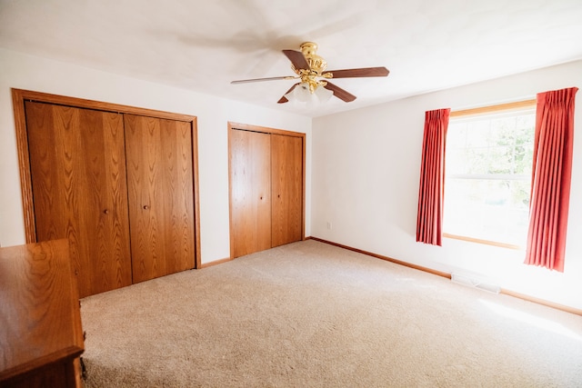 unfurnished bedroom featuring multiple closets, ceiling fan, and carpet