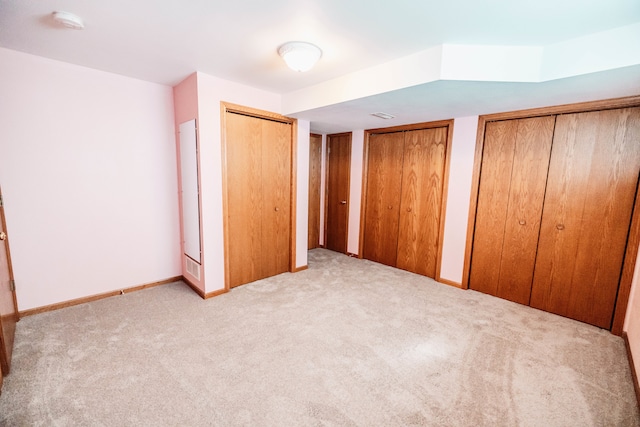 unfurnished bedroom featuring multiple closets and light colored carpet