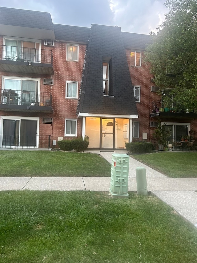 view of front facade with a balcony, a front yard, and an AC wall unit